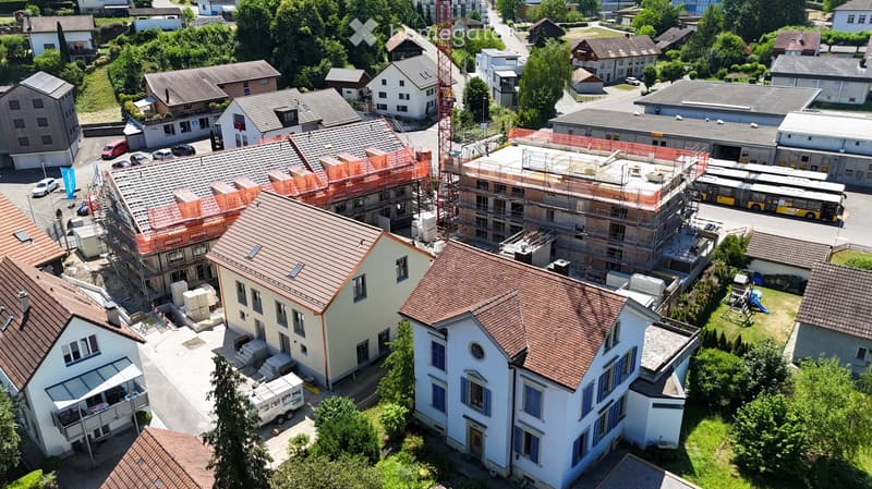 Aerial view of a residential area with multiple houses, some under construction, surrounded by greenery and a few parked cars.