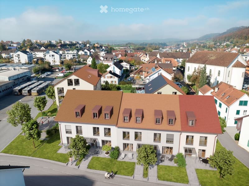 Aerial view of a residential area with a large white building with a brown roof, multiple windows, and a small garden in front.