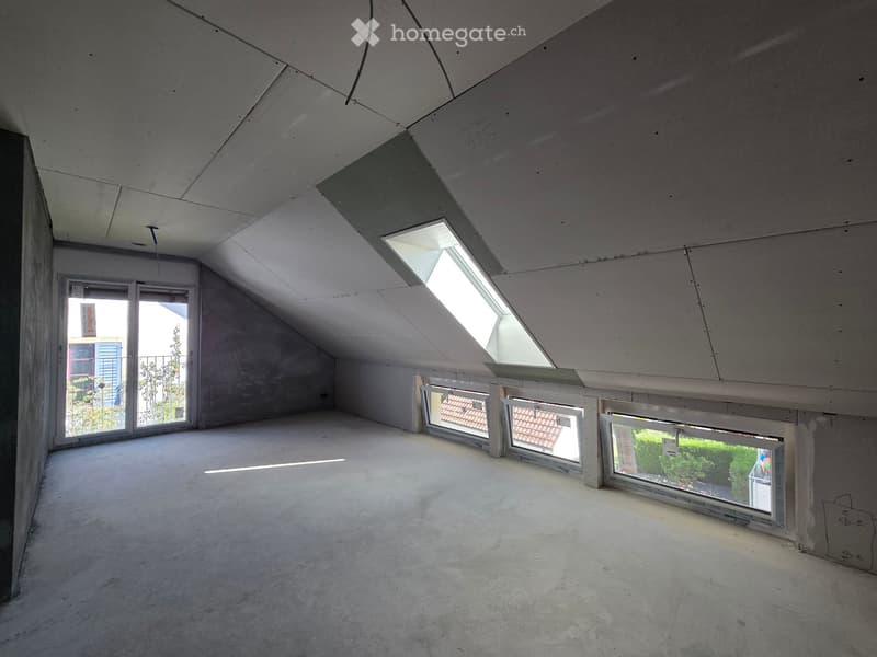 Empty attic space with concrete floors, exposed ceiling beams, and multiple skylights and windows allowing natural light.