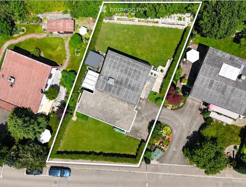Aerial view of a residential property with multiple buildings, including a main house, a garage, and outbuildings, surrounded by well-maintained gardens and lawns.