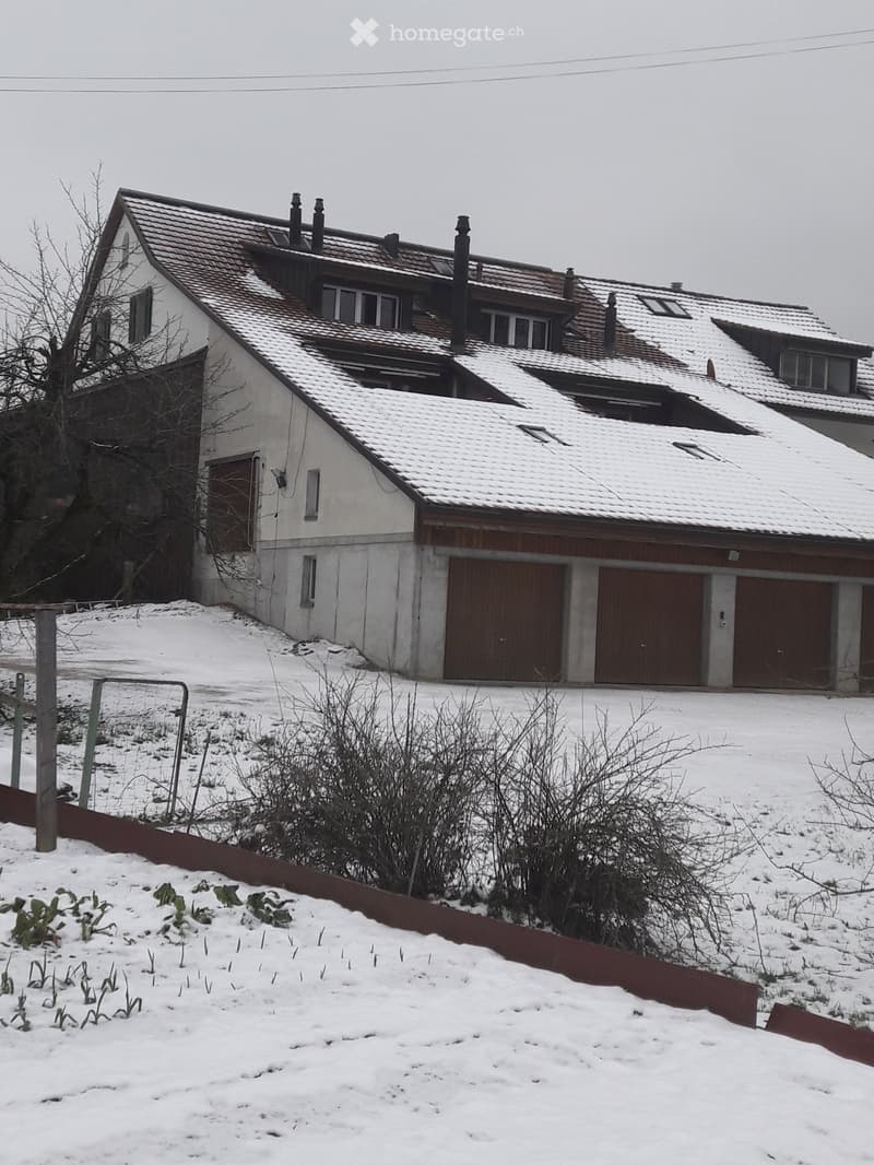 Two-story house with a tiled roof, multiple chimneys, and a garage section covered in snow.