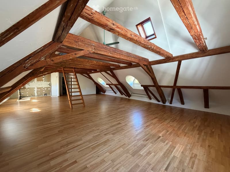 Empty attic space with wooden beams, wooden floor, and skylight windows. Ladder leads to another area.