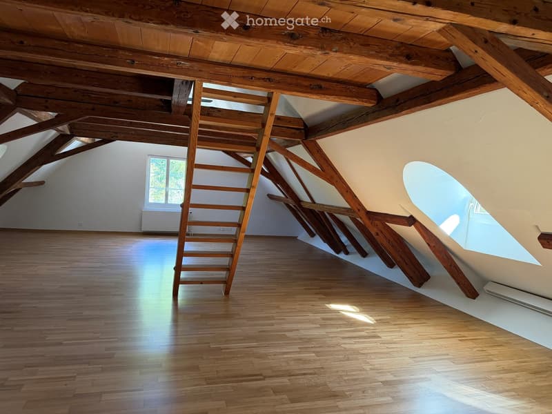 Empty attic space with exposed wooden beams, wooden floor, and skylight windows allowing natural light.