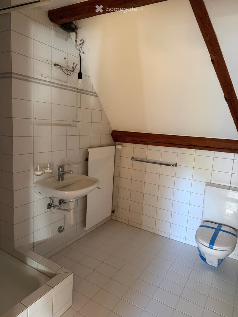 Small bathroom with white tiles, a sink with a faucet, a toilet with a blue protective cover, and two cups on the sink counter.