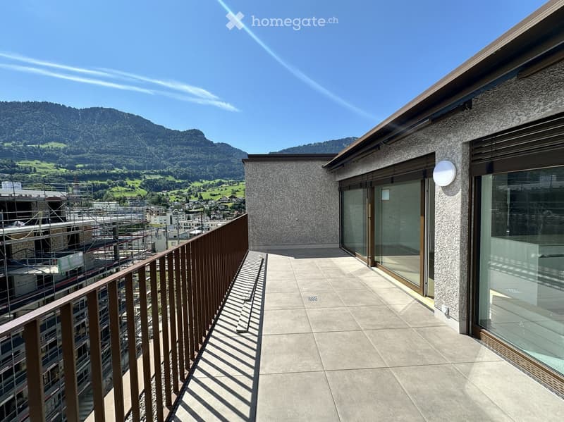 Balcony with modern glass doors, wooden railing, and a scenic mountain view in the background.