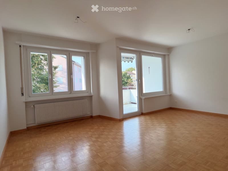 Empty room with wooden flooring, large windows, radiator, and white walls.