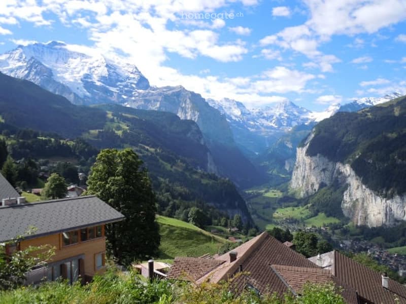 Alpine landscape with houses, valley, mountains and snow.