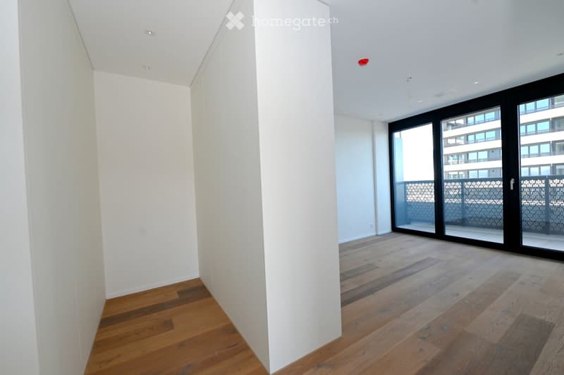 Empty room with white walls, wooden flooring, and large sliding glass doors leading to a balcony.
