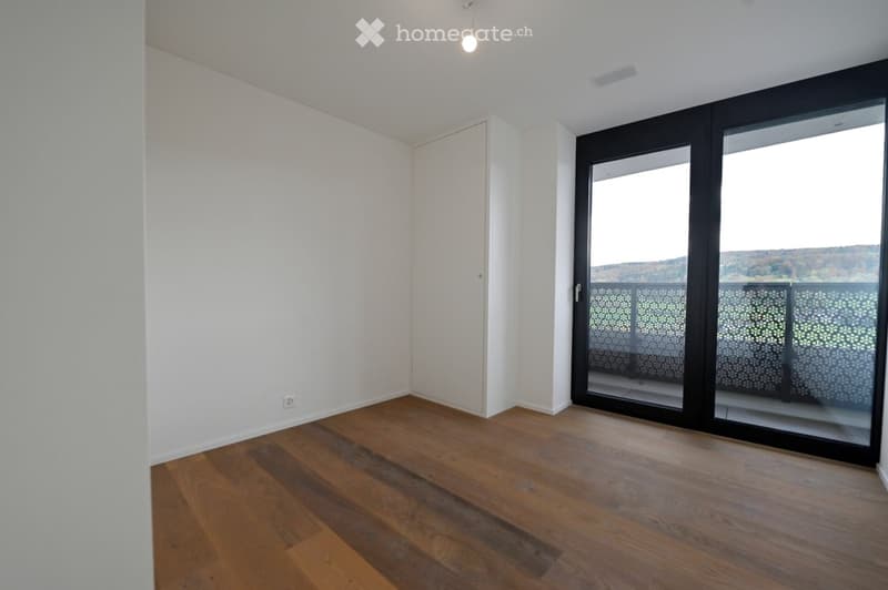 Empty room with wooden flooring, white walls, and large sliding glass doors leading to a balcony with a scenic view.