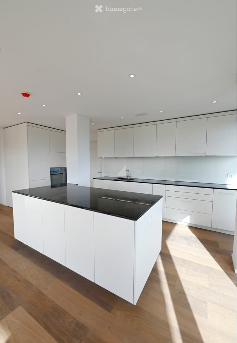 Modern kitchen with white cabinets, black countertops, and a central island. Features include a sink, oven, and recessed lighting.
