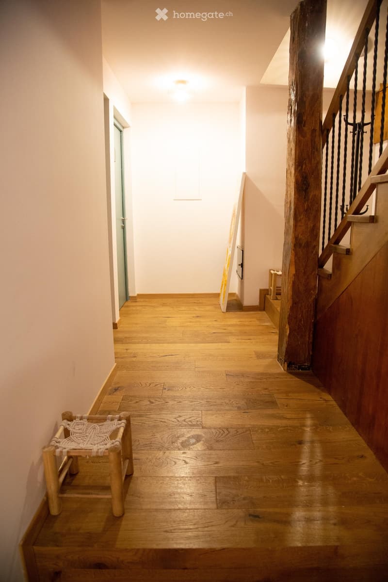 Wooden floor hallway with a staircase featuring a wooden railing and a small woven bench on the left side.