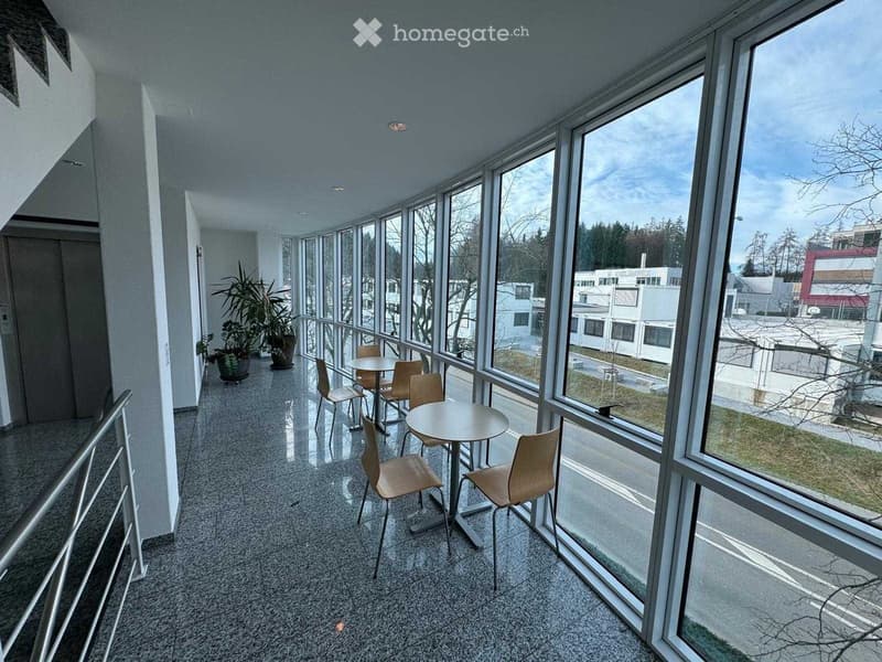 Balcony with large windows, tiled floor, small seating area with tables and chairs, and potted plants.