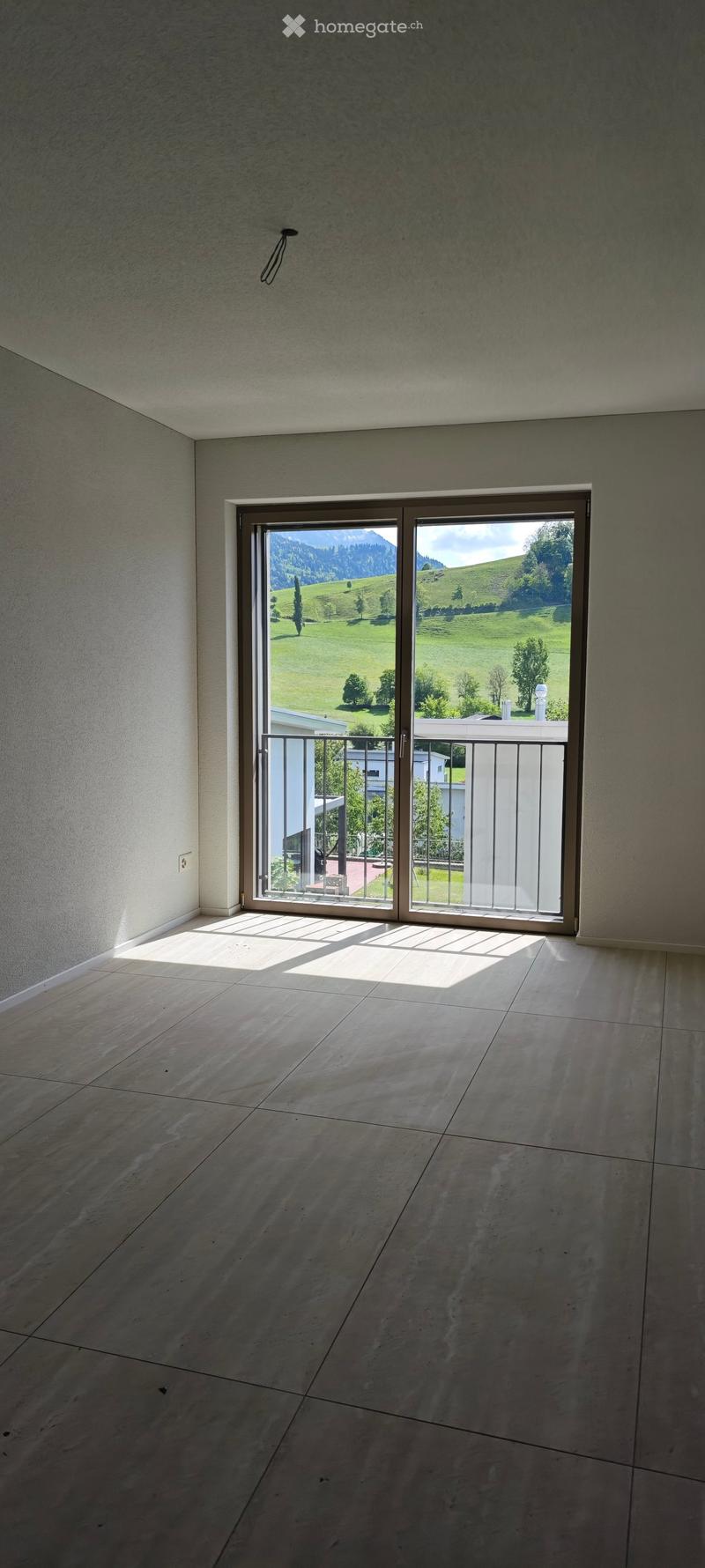 Empty room with large sliding glass doors leading to a balcony, tiled floor, and natural light from the view of green hills and mountains.