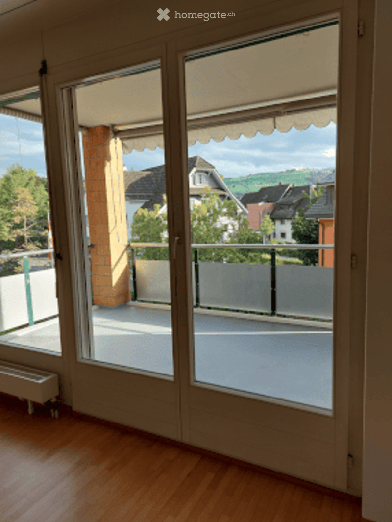 Balcony with white floor, metal railing, and view of houses and greenery.