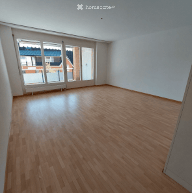 Completely empty room with wooden flooring and large windows, no furniture or equipment.