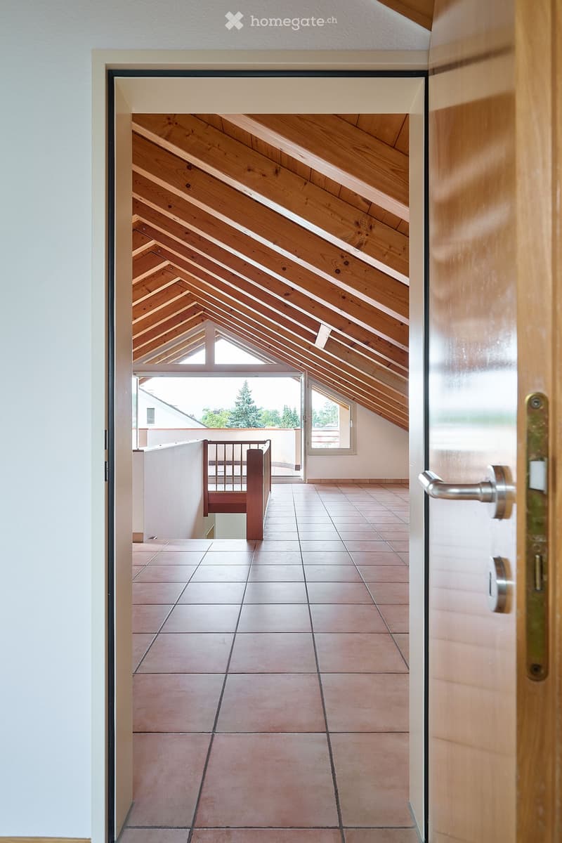 View of a hallway leading to an attic space with wooden slanted ceilings and tiled floors.