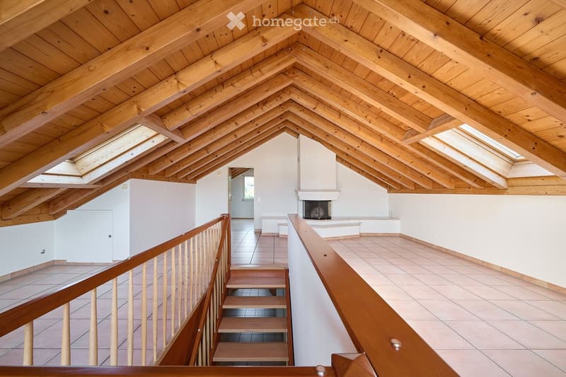 Spacious, open corridor with wooden beams and skylights, leading to a staircase and a fireplace area.