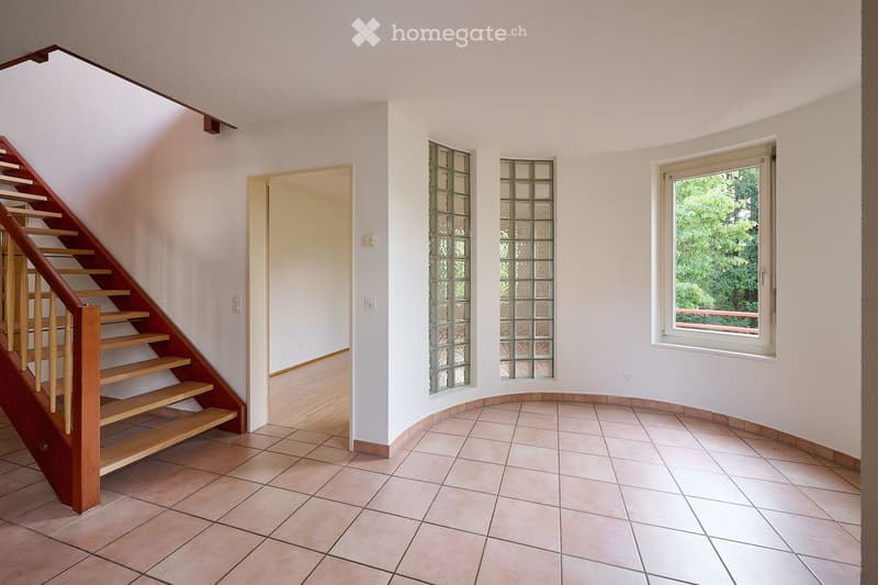 Empty hallway with tiled floor, wooden staircase, frosted glass windows, and a doorway leading to another room.