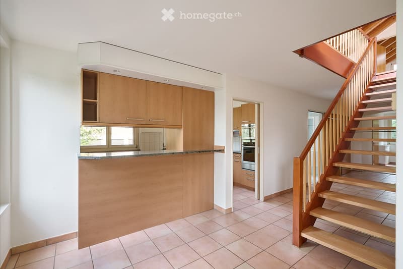Modern kitchen area with a wooden island, built-in cabinets, and a staircase leading to an upper level.