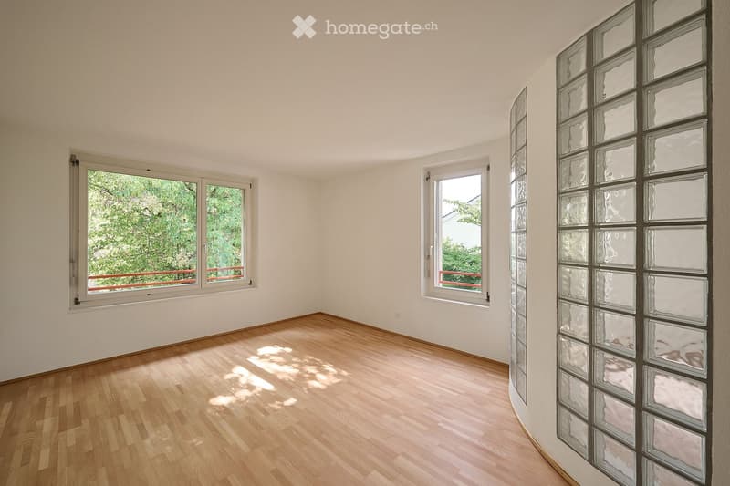 Empty room with wooden flooring, white walls, and large windows with views of greenery. No furniture or equipment present.