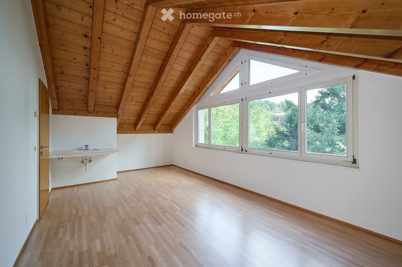 Empty room with wooden floor, white walls, and large windows with wooden frames. A small sink is visible on one wall.