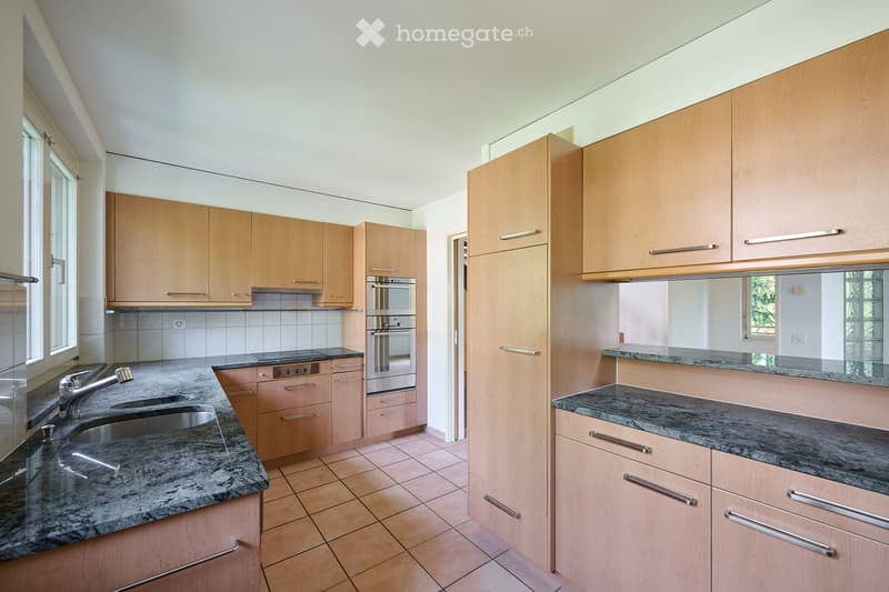 Modern kitchen with light wooden cabinets, granite countertops, stainless steel sink and faucet, and built-in oven.