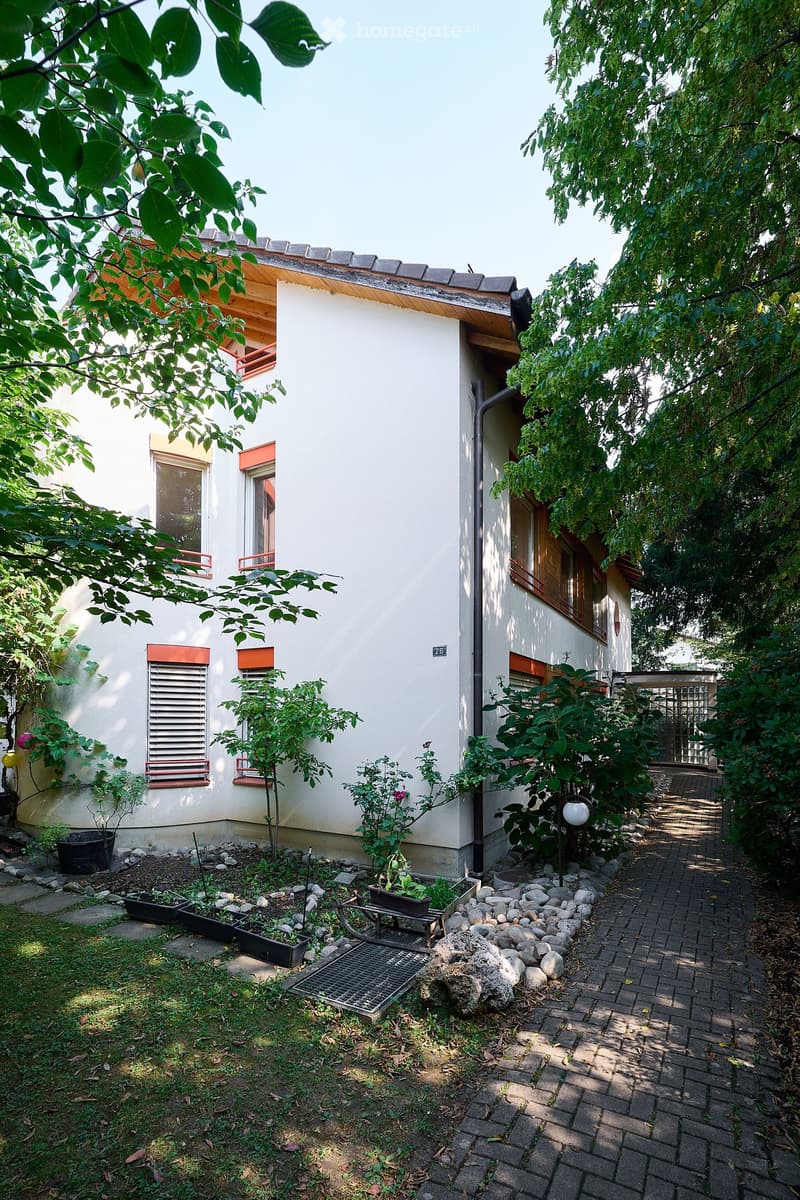 A small garden area with a bench, potted plants, and a brick pathway leading to the house entrance.