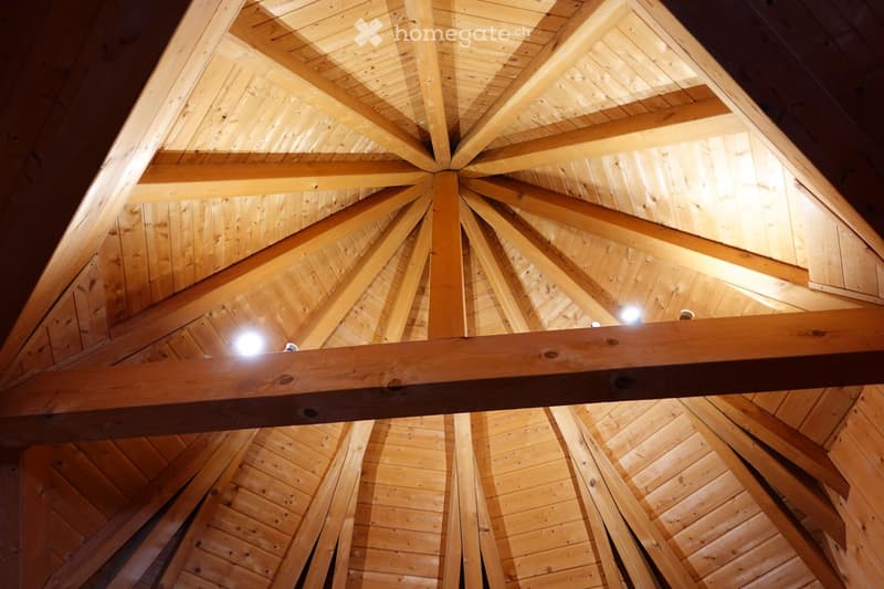 An empty room with exposed wooden beams and a wooden ceiling, illuminated by spotlights.