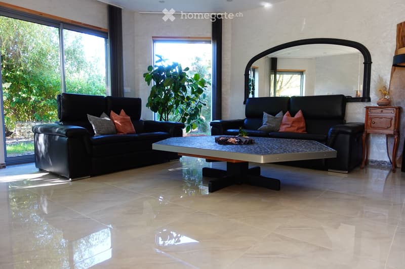 Modern living room with two black leather sofas, a glass coffee table, a large mirror, a side table, and a potted plant near the window.