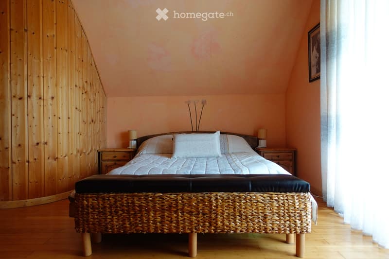 Cozy bedroom with a wooden bed, white bedding, nightstands, a woven stool, and a picture frame on the wall.