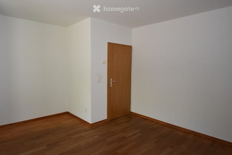 Empty room with white walls, wooden floor, and a single wooden door.