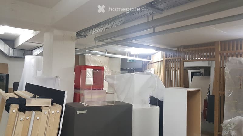 Empty room with exposed ceiling beams, various furniture pieces covered in plastic wrap, and storage items scattered around.