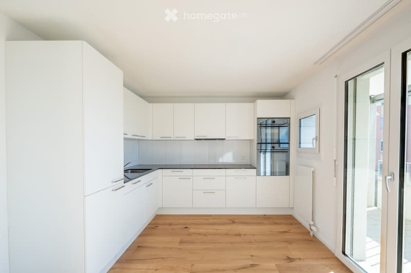 Modern, minimalist kitchen with white cabinets, wooden flooring, and a built-in oven.
