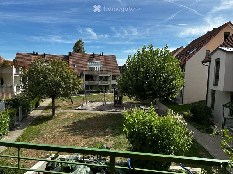 Courtyard view with green spaces, trees, pathways, and residential buildings in the background.