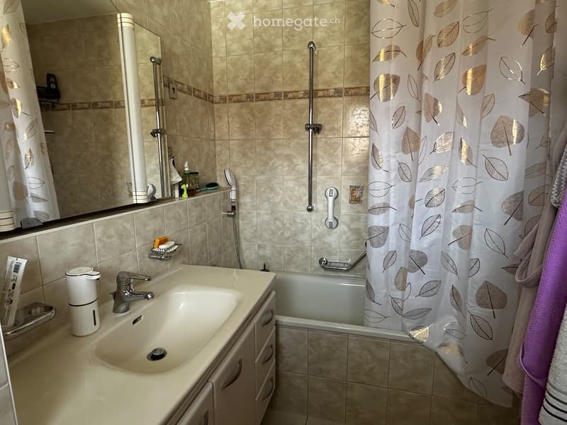 Bathroom with a sink, bathtub, shower curtain, and various toiletries. Beige tiles and a modern design.