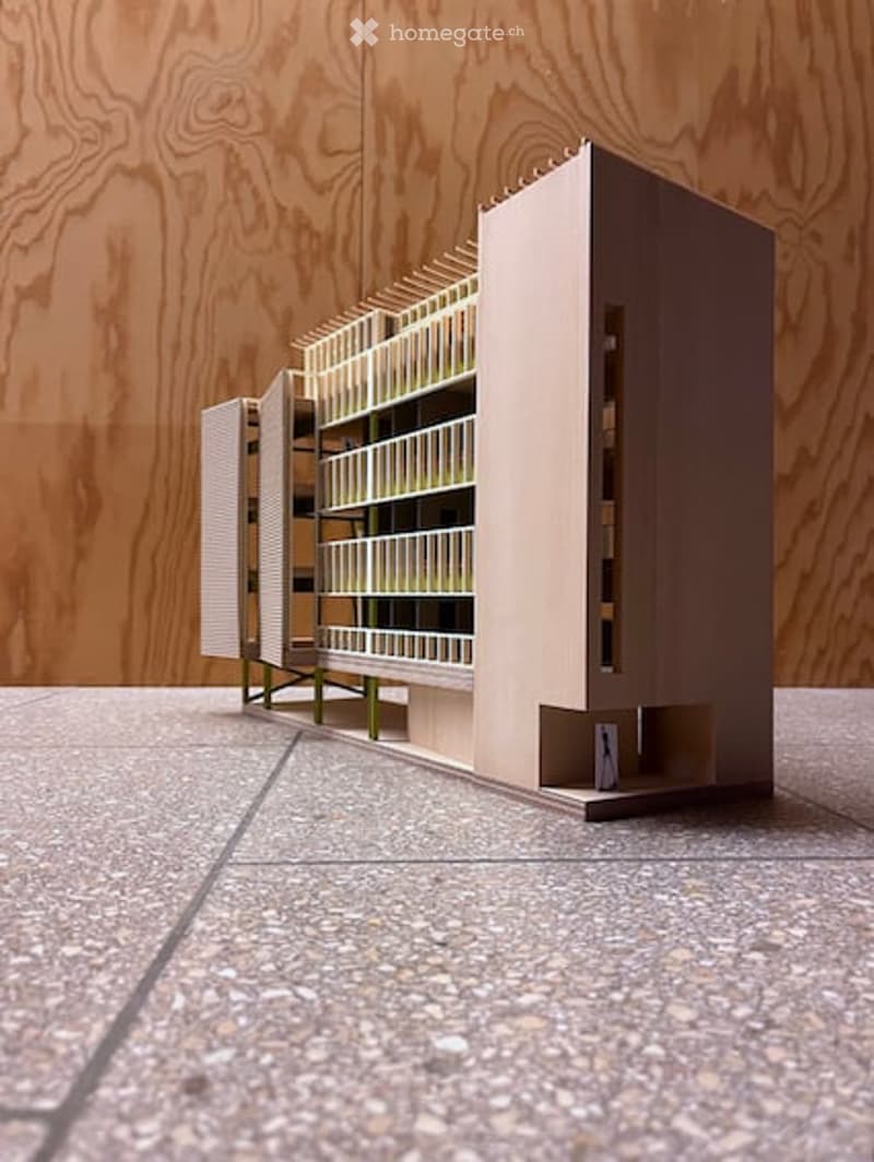 Architectural model of a multi-story building with open shelving units and a staircase, displayed on a tiled floor against a wooden wall.