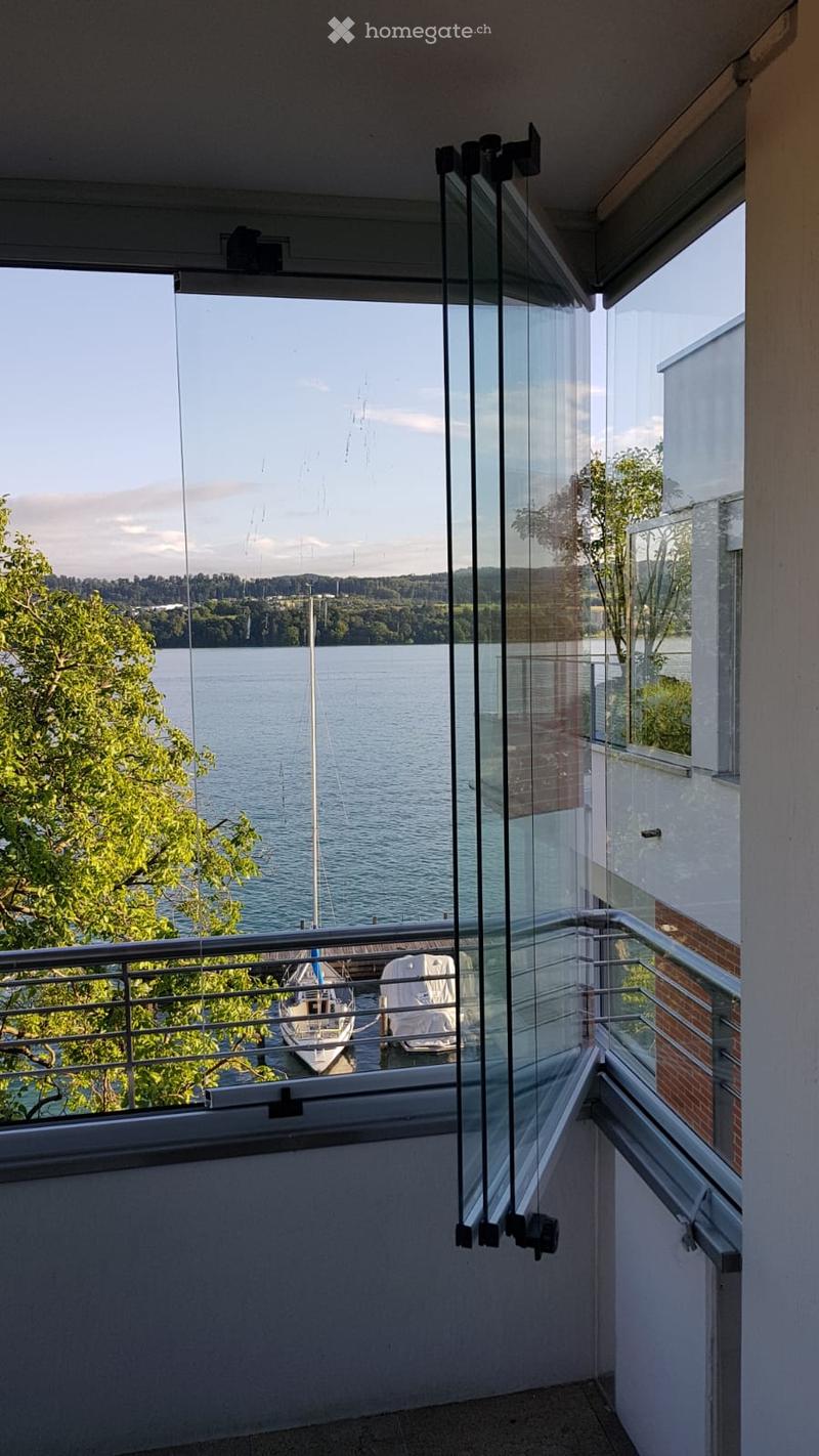Balcony with glass sliding doors, metal railing, overlooking a waterfront with boats and trees.