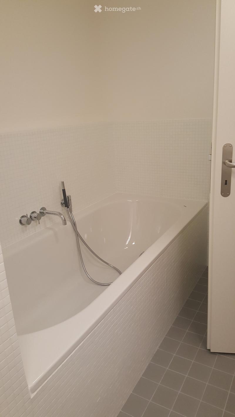 Modern bathroom with a white bathtub, chrome faucet, and tiled walls and floor.