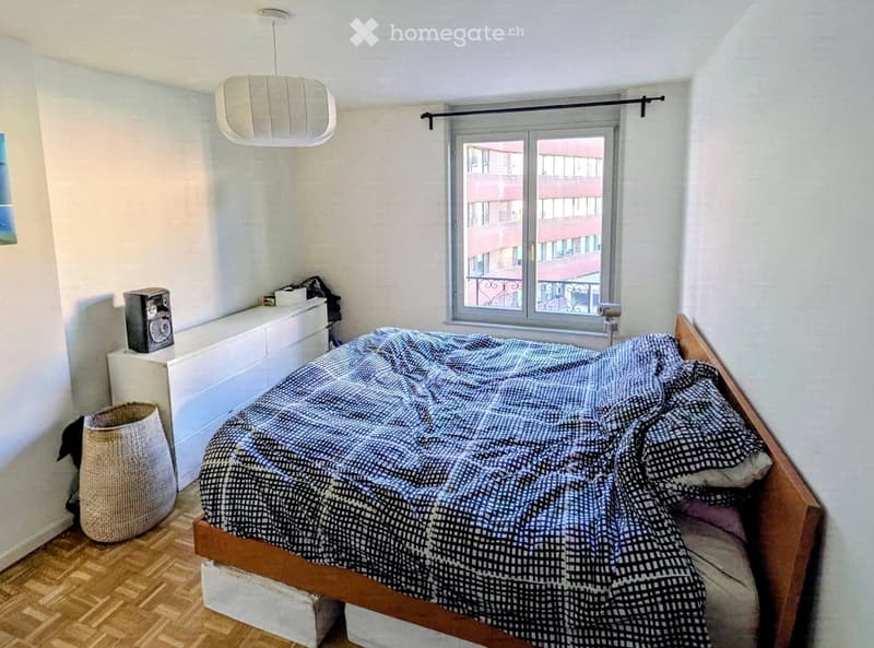 Bedroom with a wooden bed, patterned duvet, nightstand, lamp, and a woven basket on the floor.
