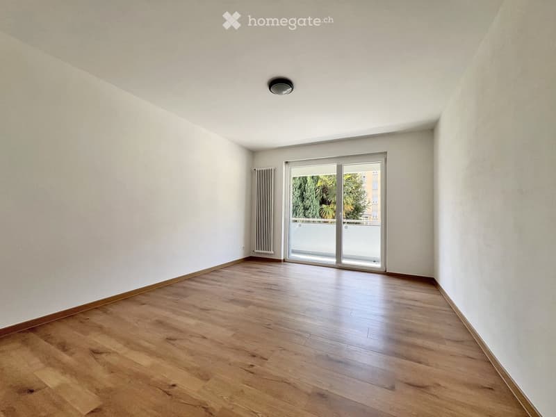 Empty room with wooden flooring, white walls, and a sliding glass door leading to a balcony.