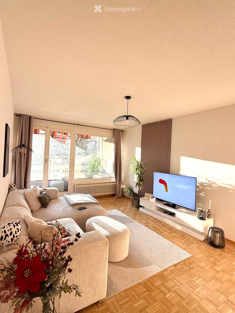 Modern living room with a sectional sofa, ottoman, coffee table, television, and decorative elements including a flower arrangement and lamps.