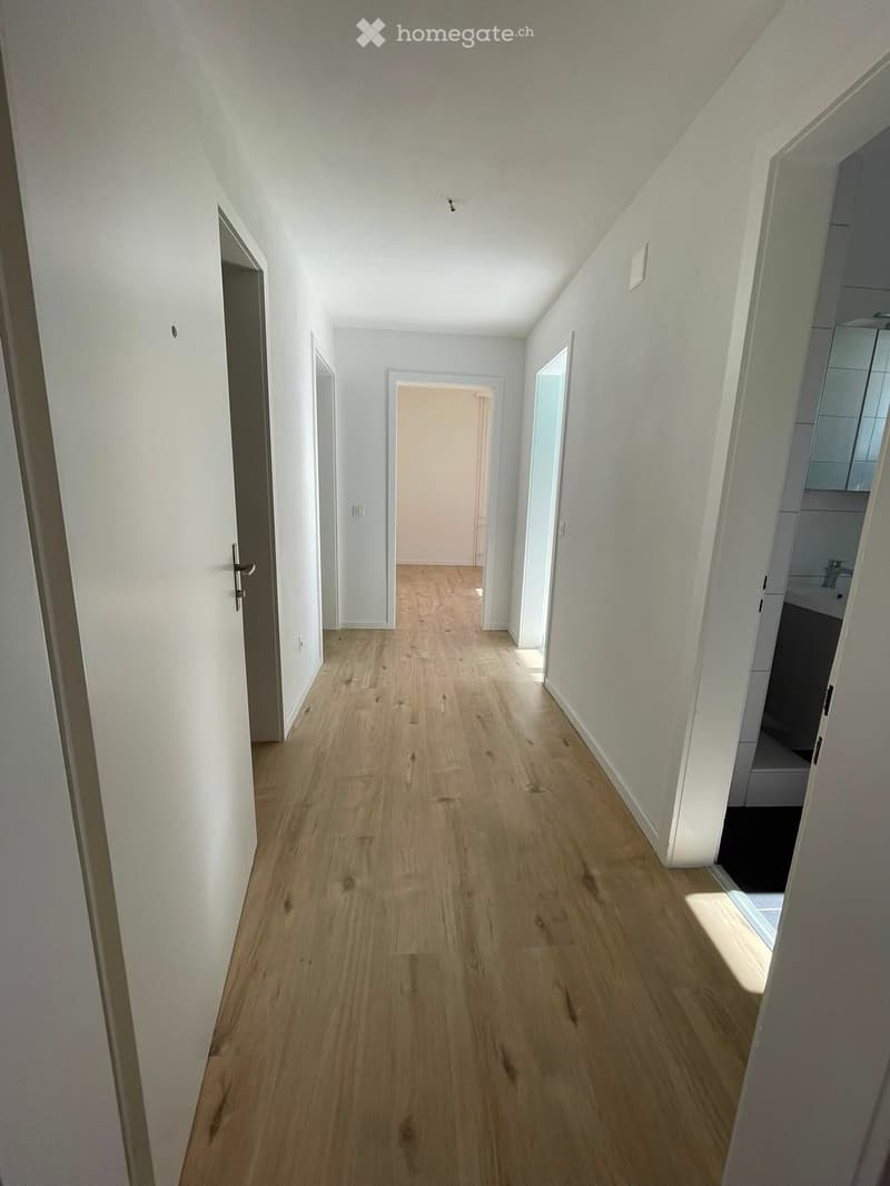 Empty hallway with light wooden flooring, white walls, and several doors leading to other rooms.