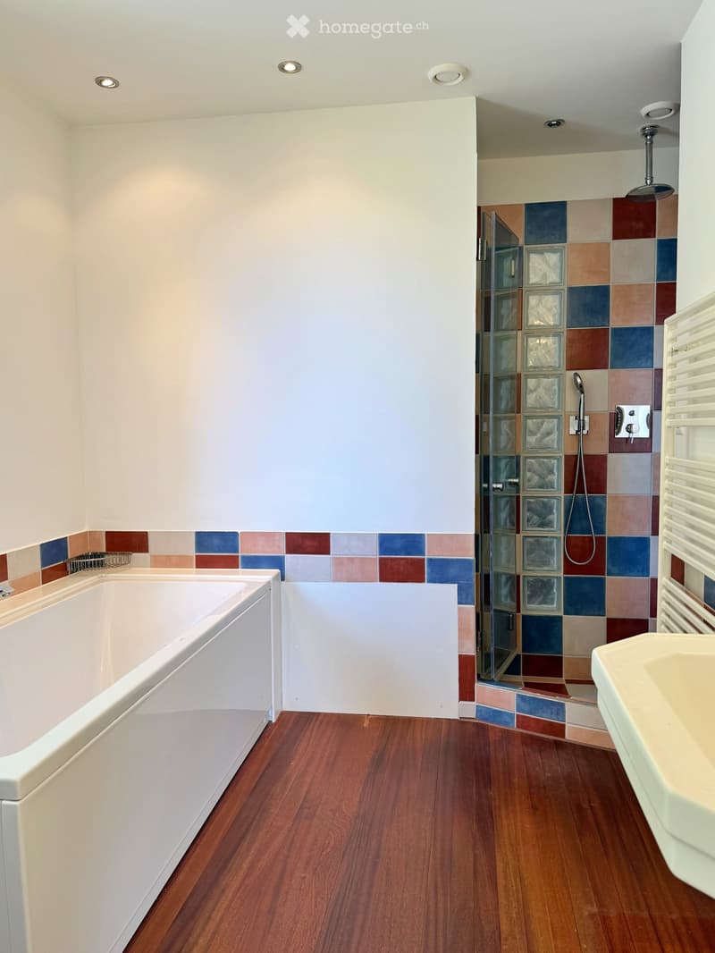 bathroom with wooden floor, bathtub, shower, colored tiles, white wall, built-in sink, and towel rack