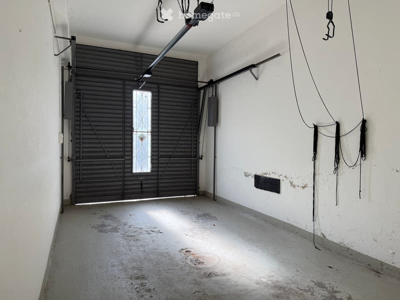 empty room with a large black door, floor with a manhole cover, white walls, ceiling with lights and metal fixtures