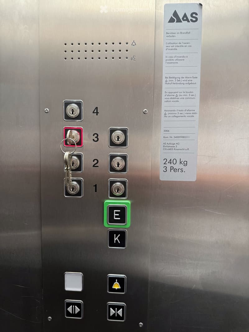 Silver elevator panel with number buttons 1-4 and emergency buttons, elevator keys attached, weight capacity of 240 kg and 3 persons.