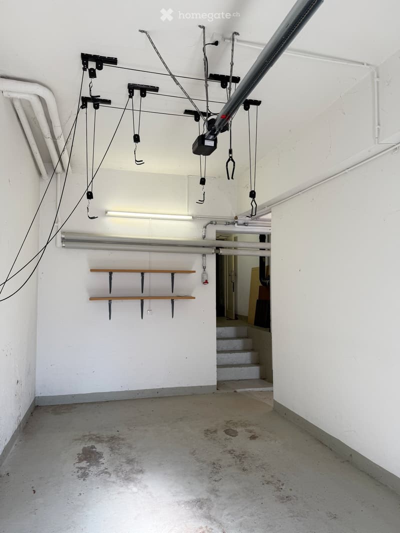 an empty garage with metal shelves, electrical cables and pipe systems