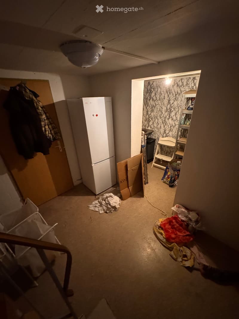 Empty room with a refrigerator, scattered items, and a partially open closet with shelves. The space appears to be in transition or storage.
