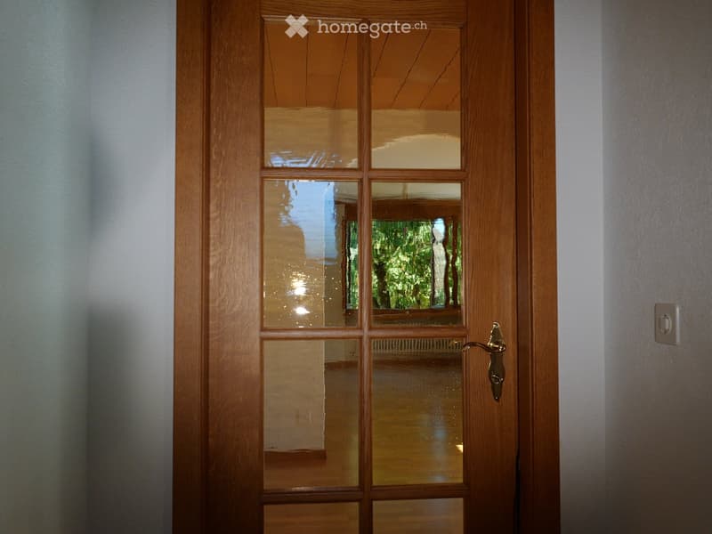 Wooden door with glass panels, brass handle, and light switch visible on the wall.