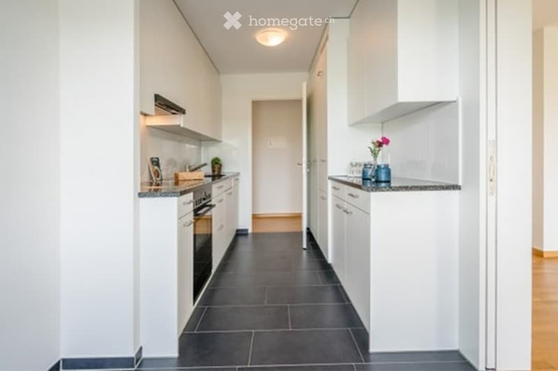 Modern kitchen with white cabinets, dark tiled floor, granite countertop, and small decorative items.