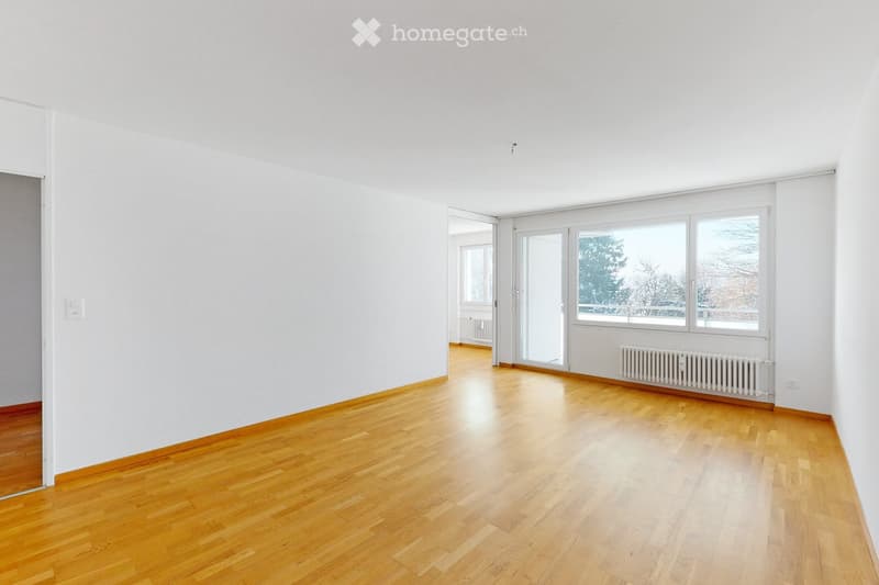 Empty room with light wooden flooring, white walls, large windows, and radiators. No furniture or equipment present.